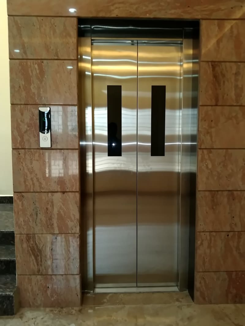 Stainless steel automatic centre-opening lift doors with vision panels set in granite cladding